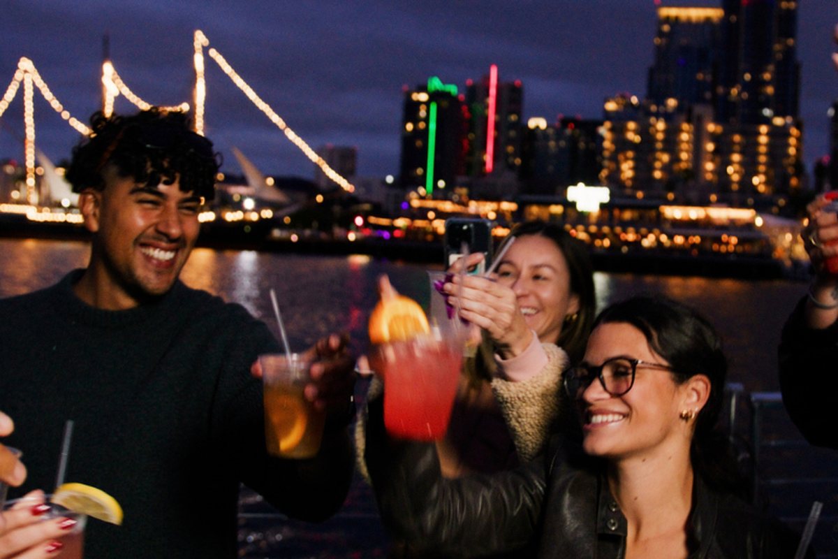 Guests raising cocktails aboard Athena at night, the lit San Diego skyline behind them