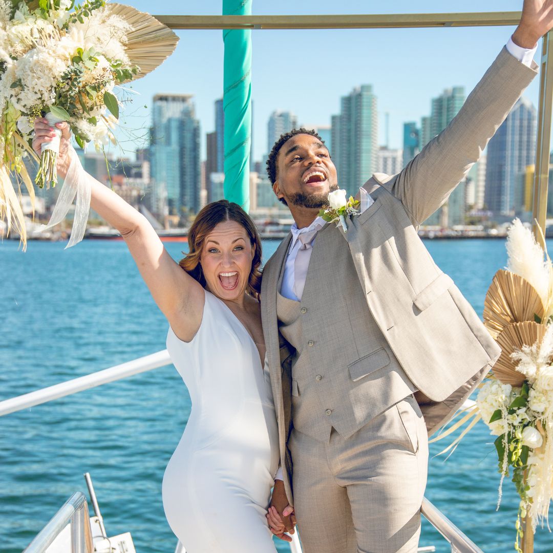 Newlyweds cheering on the bow with the San Diego skyline behind them