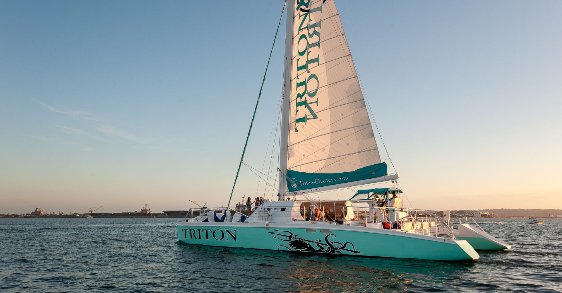 Triton, a 75-foot sailing catamaran, under sail on San Diego Bay at golden hour
