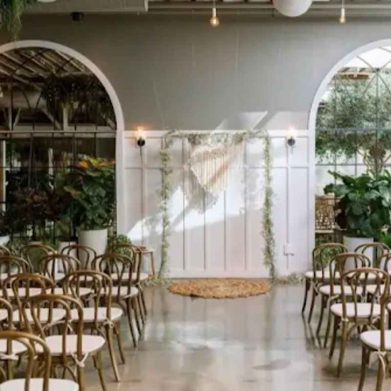 White arched event space at Flora The Venue, set with rattan chairs and hanging greenery
