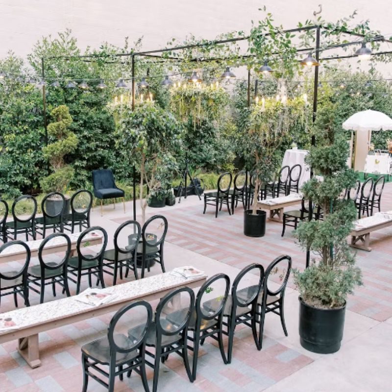The Guild Hotel’s outdoor patio, set with black bistro chairs under a pergola and potted olive trees