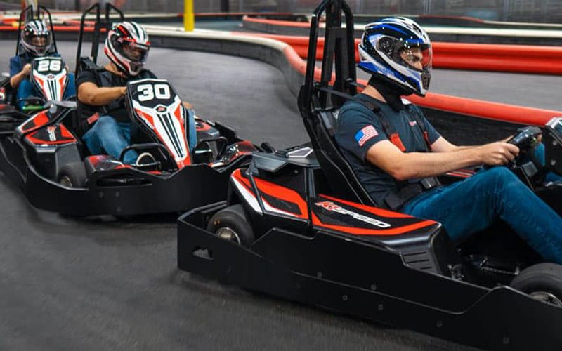 Two drivers in full-face helmets racing go-karts on an indoor track