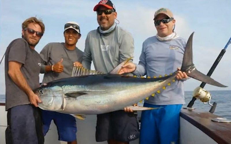 Four anglers holding up a large tuna on the deck of a sportfishing boat