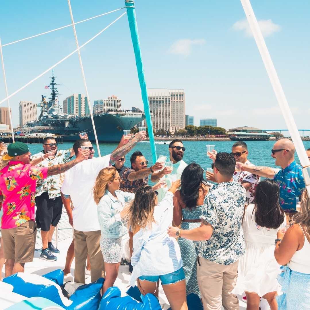 Group of friends celebrating on the Triton catamaran’s deck with the downtown skyline and USS Midway behind them