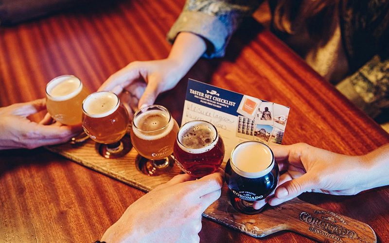 Hands reaching for a flight of craft beers on a wooden paddle board