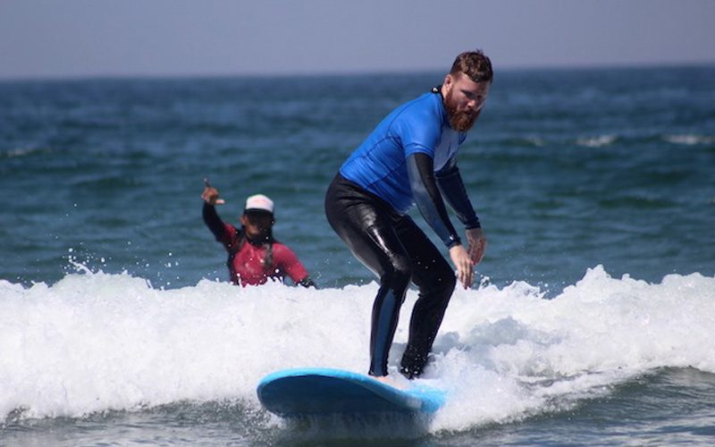 Surfer riding a small wave with an instructor watching from behind